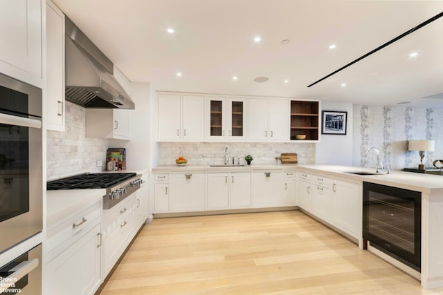 kitchen with sink, white cabinetry, beverage cooler, and wall chimney range hood