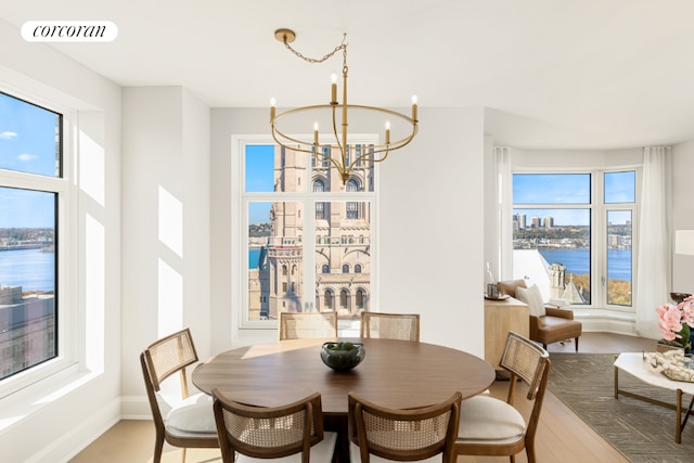 dining area featuring a water view, a healthy amount of sunlight, wood-type flooring, and a notable chandelier