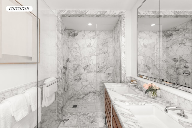 bathroom featuring a sink, a marble finish shower, and double vanity