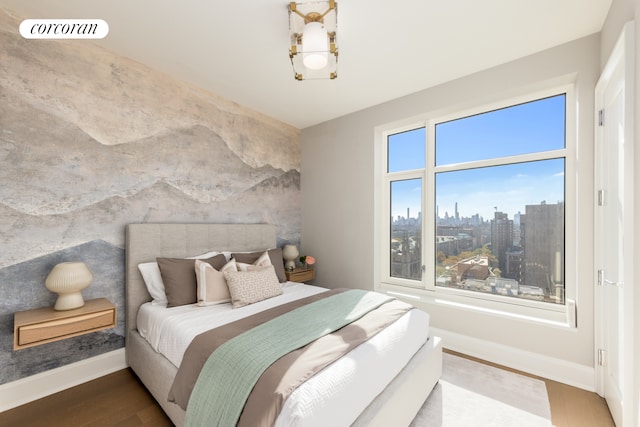 bedroom featuring an accent wall, wood finished floors, visible vents, baseboards, and a view of city