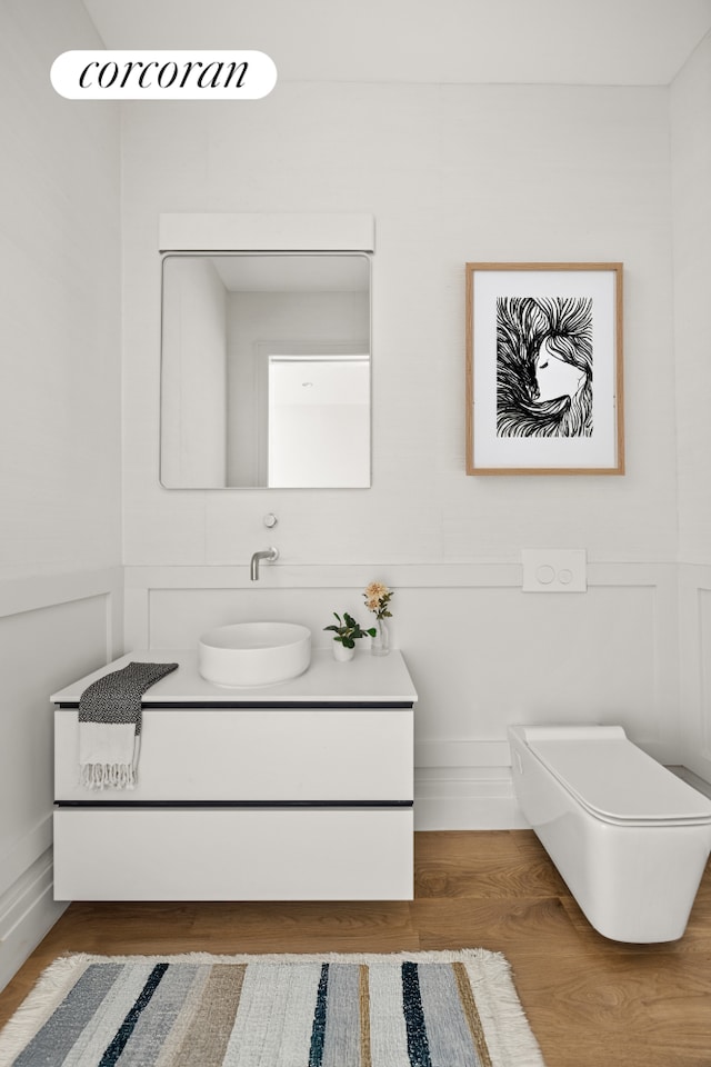 bathroom featuring a decorative wall, wainscoting, vanity, and wood finished floors