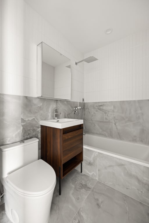 bathroom with toilet, vanity, marble finish floor, tile walls, and tiled shower / bath