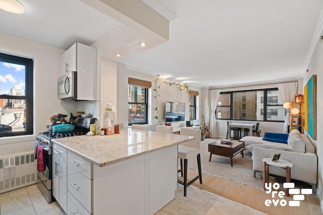 kitchen featuring radiator, appliances with stainless steel finishes, open floor plan, white cabinets, and a kitchen bar