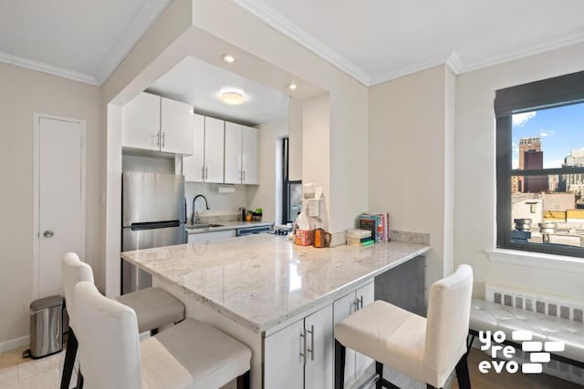 kitchen with white cabinetry, radiator, stainless steel fridge, and a kitchen bar