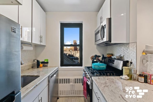 kitchen with white cabinetry, light stone counters, radiator heating unit, and stainless steel appliances