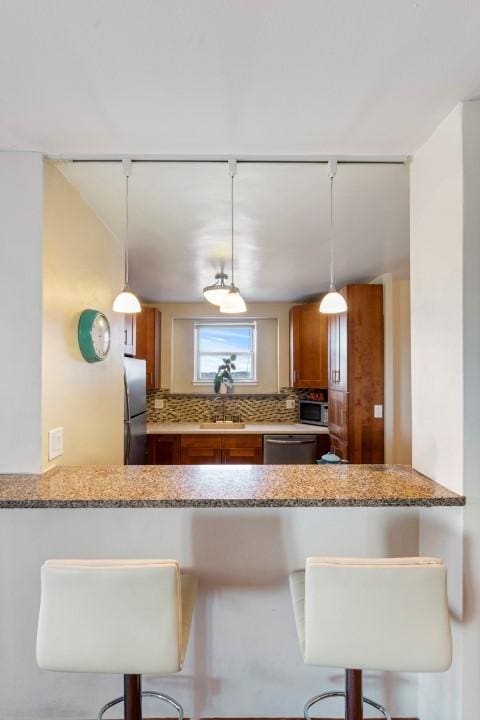 kitchen with light stone countertops, brown cabinetry, a peninsula, a sink, and appliances with stainless steel finishes