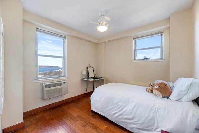 bedroom featuring baseboards, multiple windows, wood finished floors, and a wall mounted AC