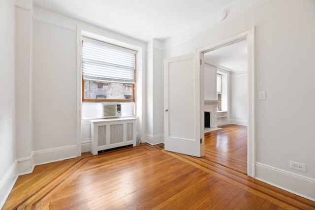 empty room with cooling unit, radiator heating unit, wood-type flooring, and plenty of natural light