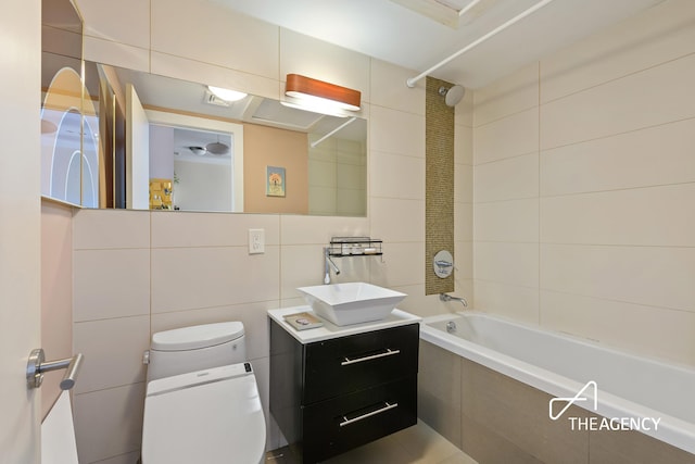 bathroom with vanity, tile walls, toilet, tiled shower / bath, and tasteful backsplash