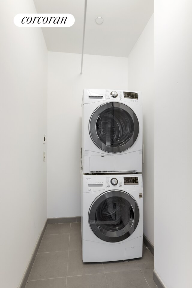 laundry area with stacked washer and dryer, tile patterned flooring, laundry area, and baseboards