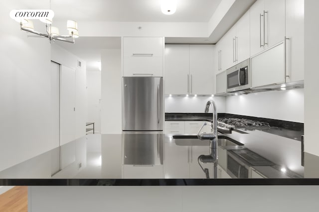 kitchen featuring a notable chandelier, stainless steel appliances, white cabinetry, dark countertops, and decorative light fixtures