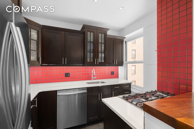 kitchen with glass insert cabinets, dark brown cabinetry, decorative backsplash, appliances with stainless steel finishes, and a sink