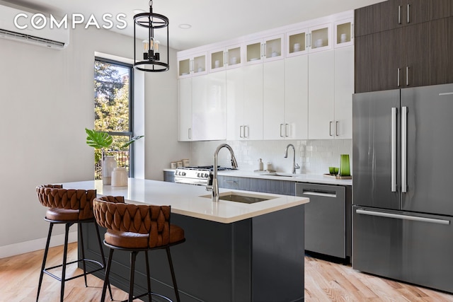 kitchen featuring a wall mounted air conditioner, light wood-type flooring, tasteful backsplash, appliances with stainless steel finishes, and light countertops