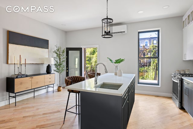 kitchen featuring a sink, stainless steel range with gas cooktop, an AC wall unit, light countertops, and dark cabinets