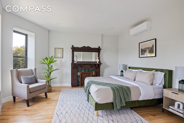 bedroom featuring baseboards, light wood finished floors, and a wall mounted AC