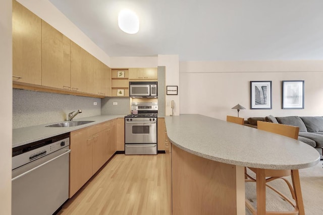 kitchen with light brown cabinetry, sink, a kitchen breakfast bar, light hardwood / wood-style floors, and stainless steel appliances