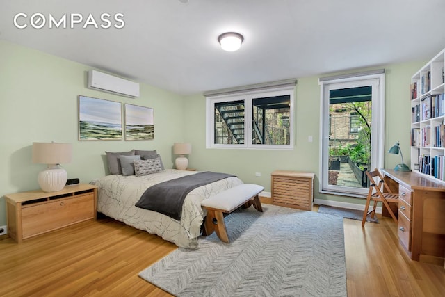 bedroom with access to exterior, light hardwood / wood-style floors, and a wall mounted AC