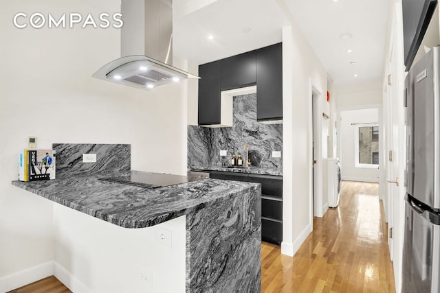 kitchen featuring black electric cooktop, island exhaust hood, stainless steel fridge, and kitchen peninsula