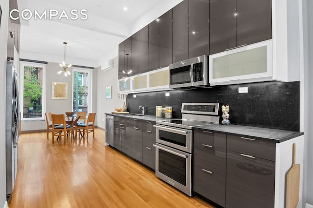 kitchen with sink, tasteful backsplash, appliances with stainless steel finishes, pendant lighting, and light hardwood / wood-style floors