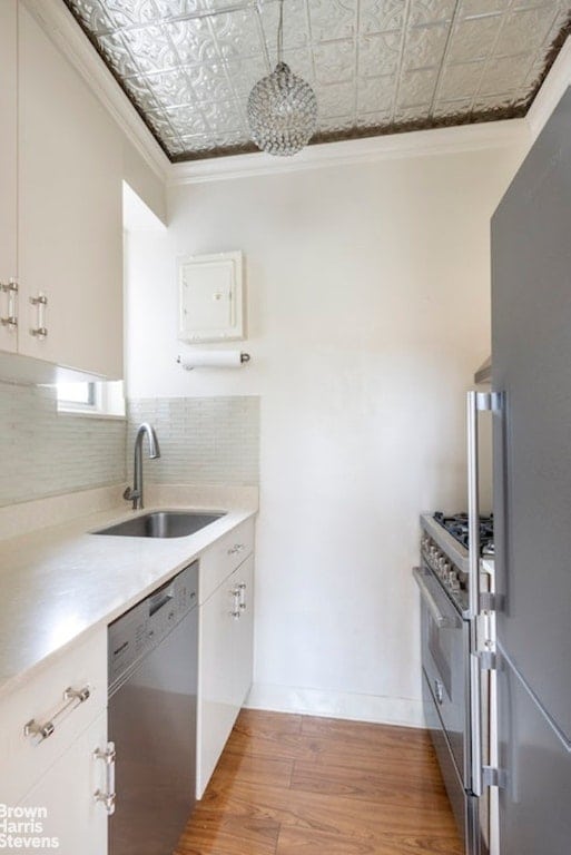 kitchen featuring sink, crown molding, stainless steel appliances, decorative backsplash, and white cabinets