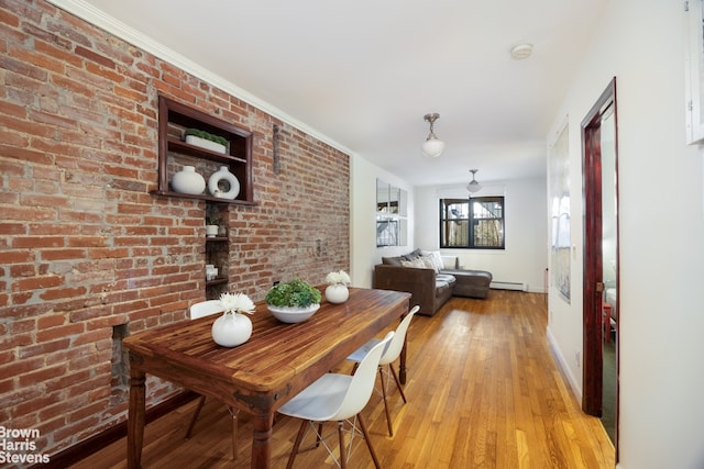 dining room featuring crown molding, a baseboard radiator, brick wall, and light wood-type flooring