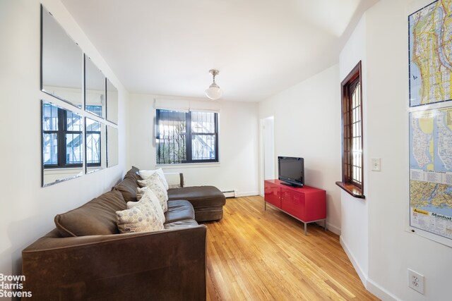 living room featuring a baseboard radiator, baseboards, and light wood-style floors