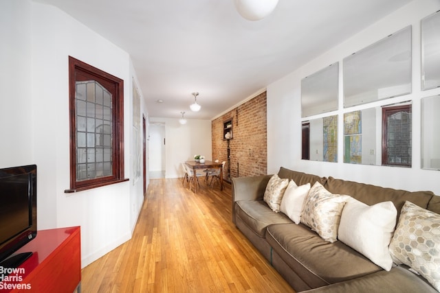 living area featuring light wood finished floors, brick wall, and baseboards