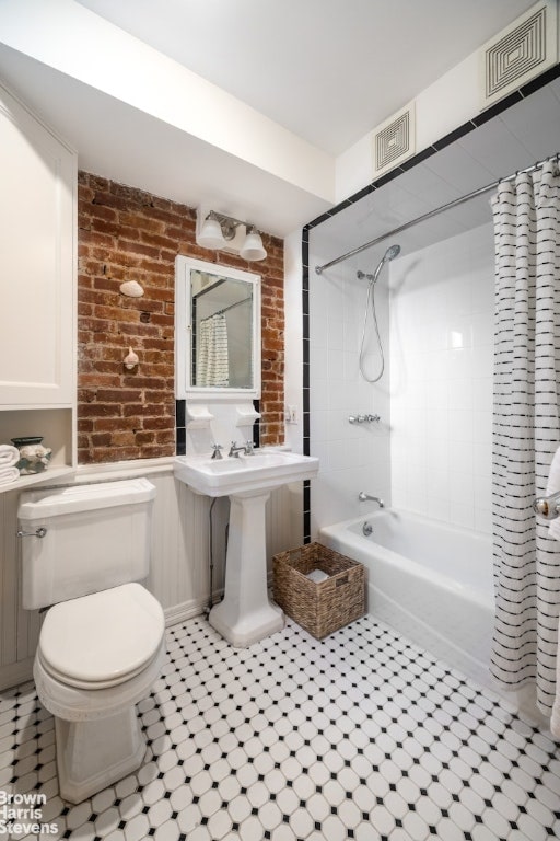 bathroom with shower / bathtub combination with curtain, toilet, and brick wall