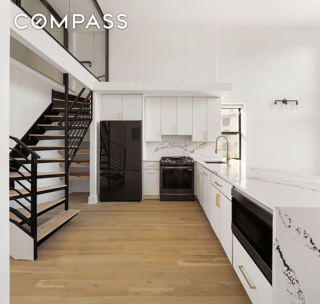 kitchen with a sink, built in microwave, white cabinetry, black fridge, and gas stove