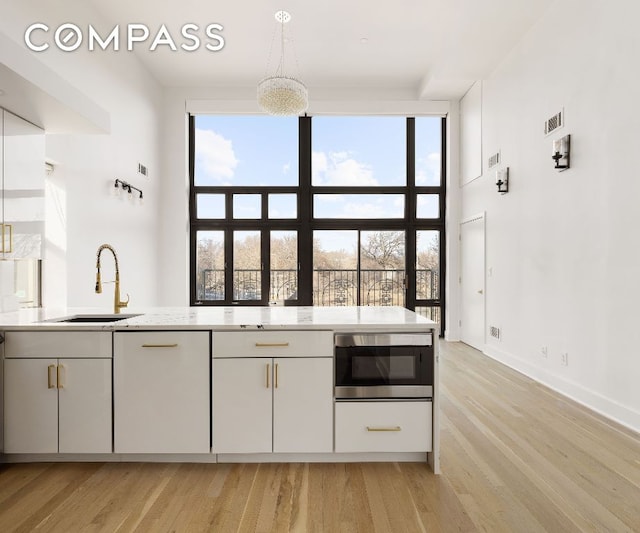 kitchen with stainless steel microwave, sink, white cabinets, hanging light fixtures, and light hardwood / wood-style flooring