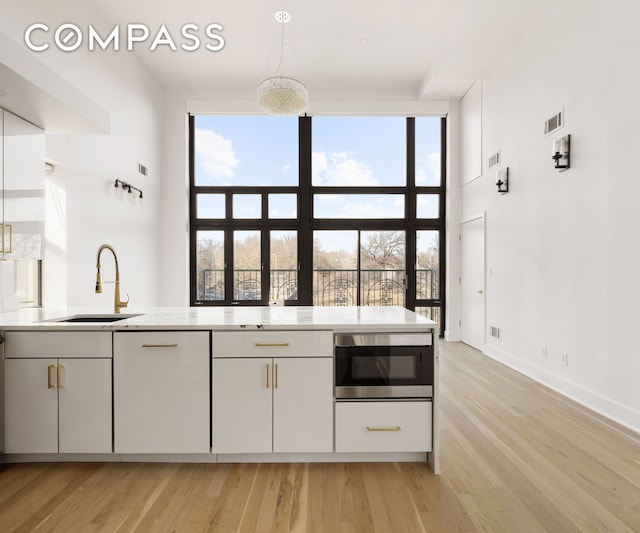 kitchen with light countertops, stainless steel microwave, visible vents, a sink, and light wood-type flooring