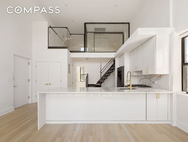 kitchen with sink, white cabinets, a high ceiling, kitchen peninsula, and light wood-type flooring