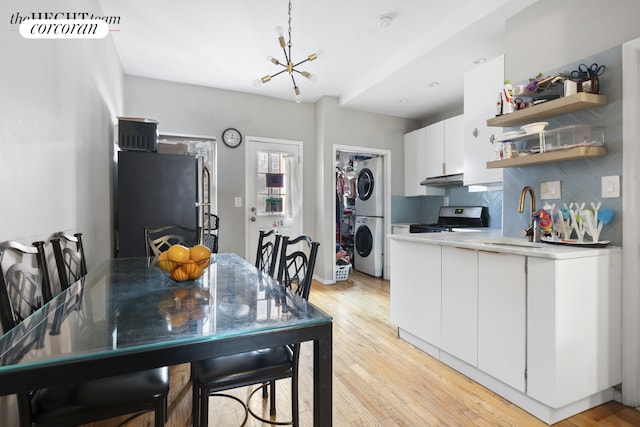 kitchen with sink, white cabinetry, stainless steel appliances, stacked washing maching and dryer, and backsplash