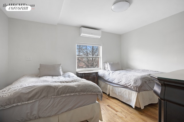 bedroom with a wall mounted air conditioner and light hardwood / wood-style floors