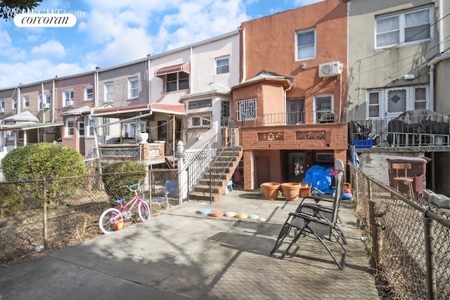 back of property featuring a wall unit AC, fence, stairway, and stucco siding