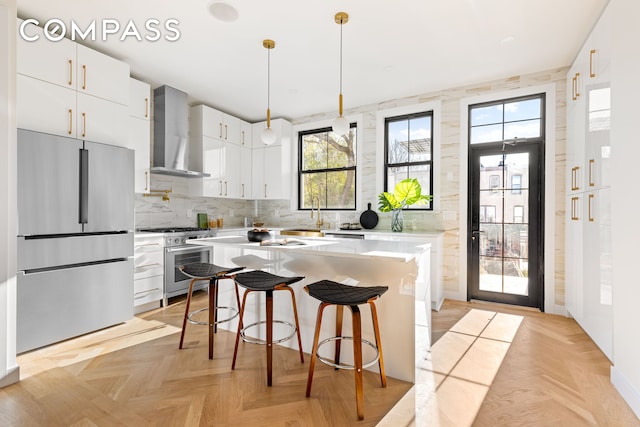 kitchen with decorative backsplash, wall chimney exhaust hood, appliances with stainless steel finishes, a kitchen breakfast bar, and light countertops