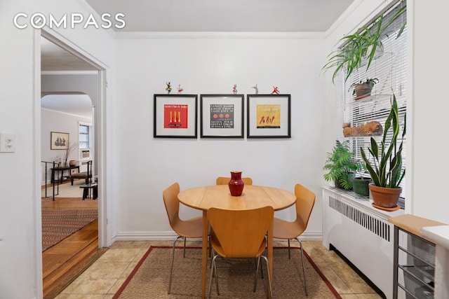 dining room with radiator, baseboards, ornamental molding, light tile patterned flooring, and arched walkways