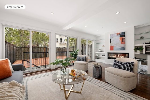 living area featuring visible vents, built in shelves, beam ceiling, wood finished floors, and a glass covered fireplace