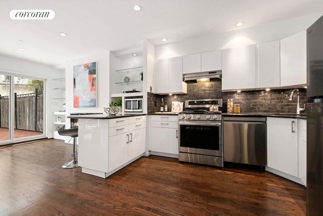 kitchen with open shelves, under cabinet range hood, appliances with stainless steel finishes, dark wood-style flooring, and a peninsula
