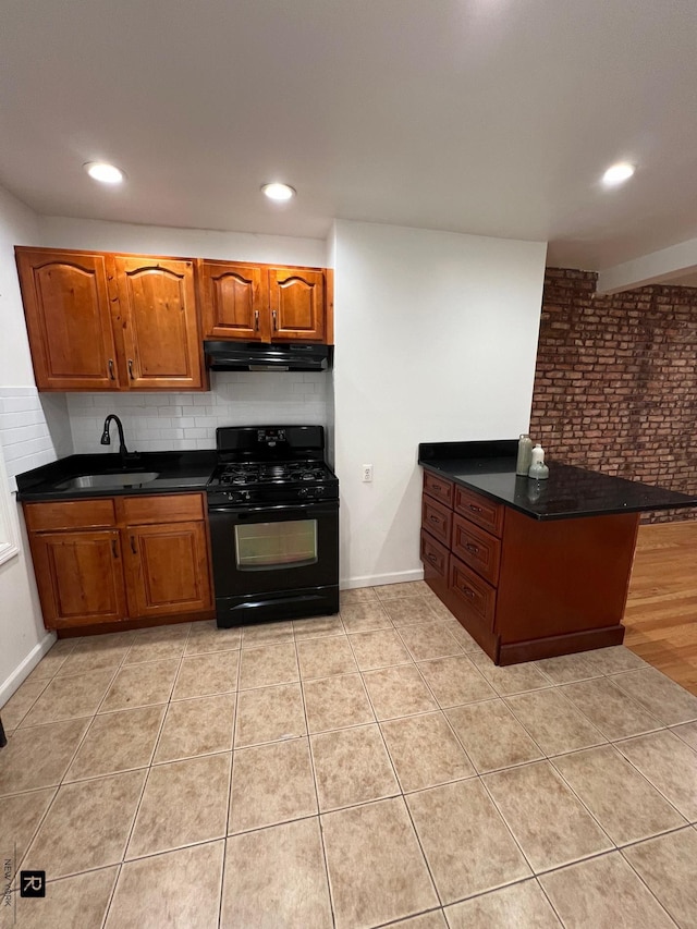 kitchen with black range with gas cooktop, dark countertops, a peninsula, under cabinet range hood, and a sink