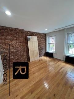 unfurnished living room with recessed lighting, wood finished floors, and brick wall