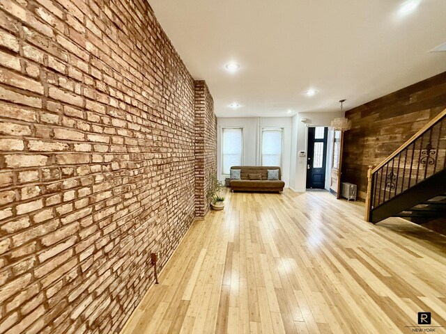 unfurnished room with recessed lighting, wood-type flooring, brick wall, and stairs