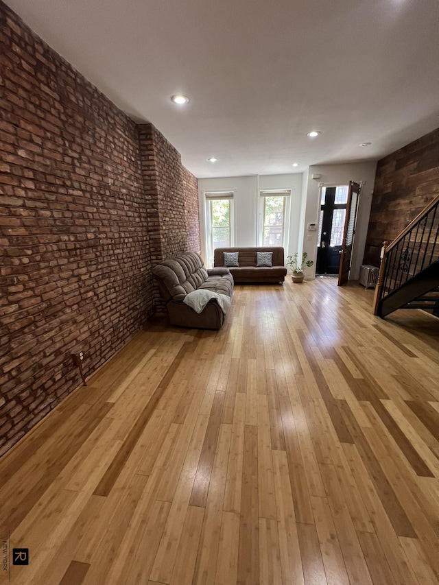 unfurnished living room featuring recessed lighting, brick wall, hardwood / wood-style floors, and stairs