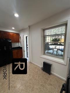 kitchen featuring black refrigerator, radiator, and light tile patterned floors