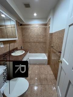 bathroom with tile walls, a tile shower, vanity, tile patterned floors, and toilet