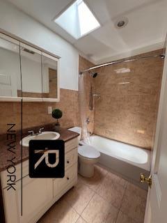 full bathroom with a skylight, tile walls, toilet, vanity, and washtub / shower combination