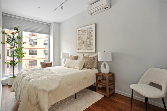 bedroom with an AC wall unit, rail lighting, baseboards, and wood finished floors