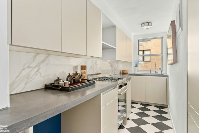 kitchen with light floors, a sink, stainless steel stove, and decorative backsplash