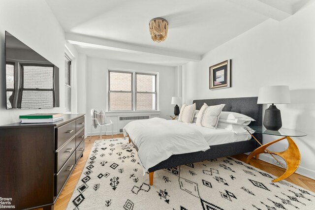 bedroom featuring beam ceiling, radiator, and light wood-type flooring