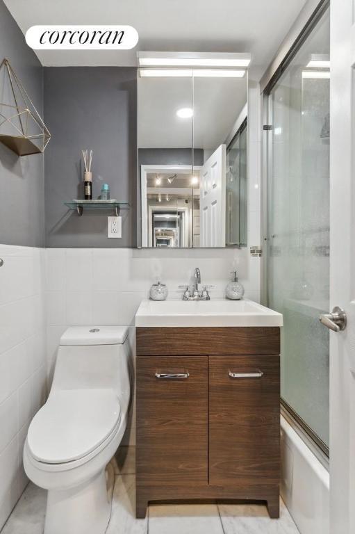 full bathroom with tile walls, vanity, bath / shower combo with glass door, and toilet